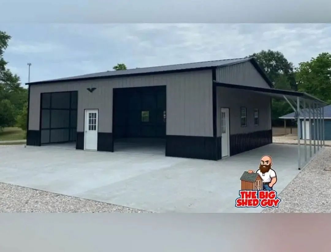 Grey and black metal workshop with two large bays, white doors, and a concrete apron.