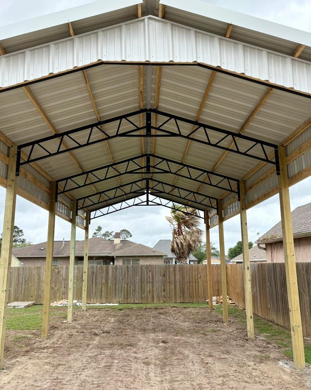 Carport with a metal roof and wooden posts in a backyard setting.