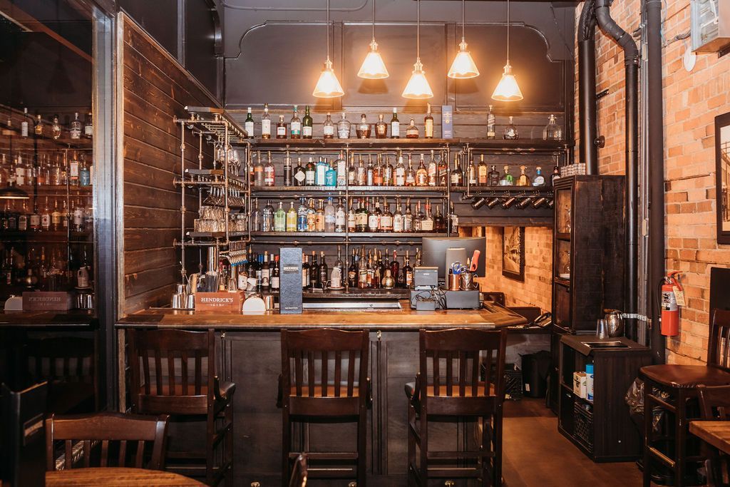 A bar with a lot of bottles on the shelves and tables and chairs