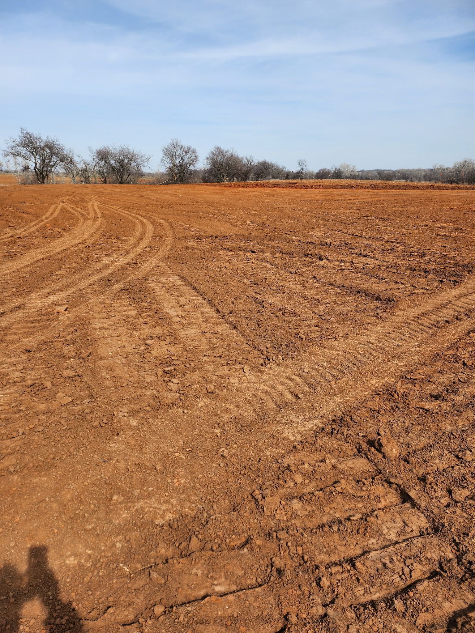 A large dirt field with trees in the background on a sunny day