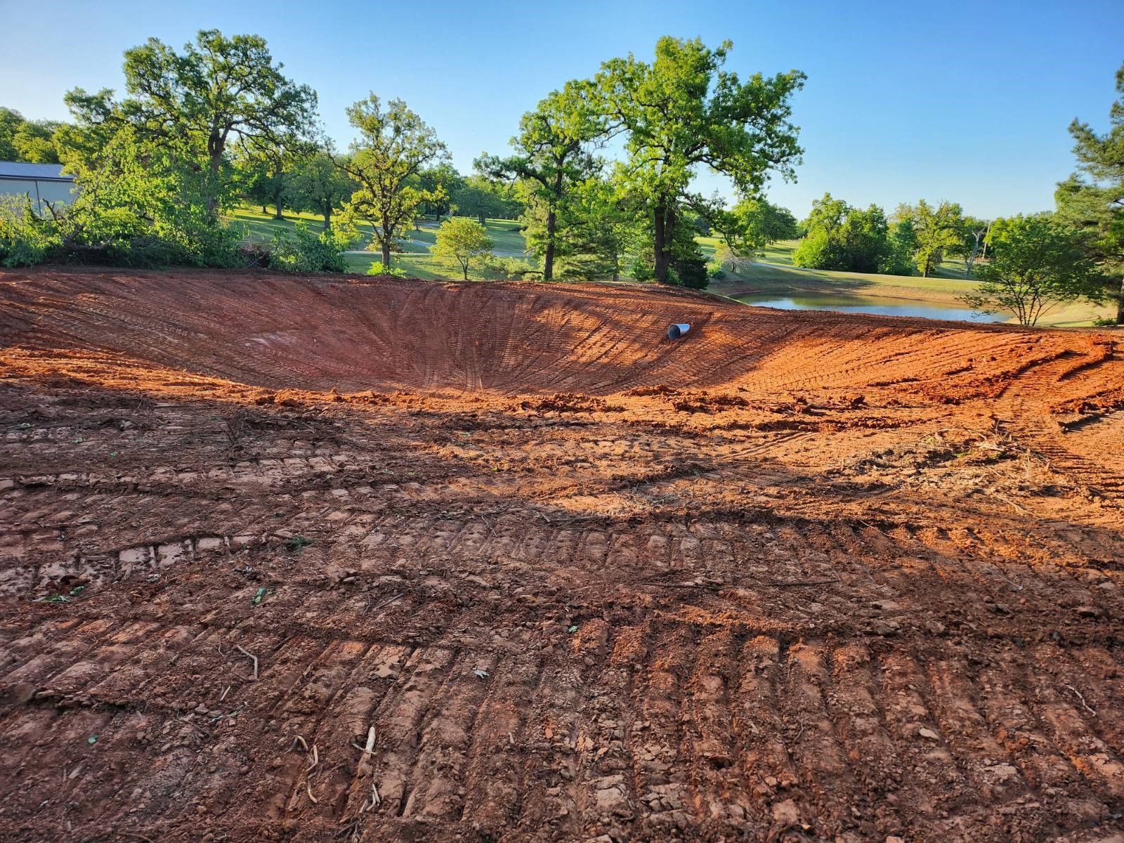 A dirt field with trees in the background and a pond in the middle.