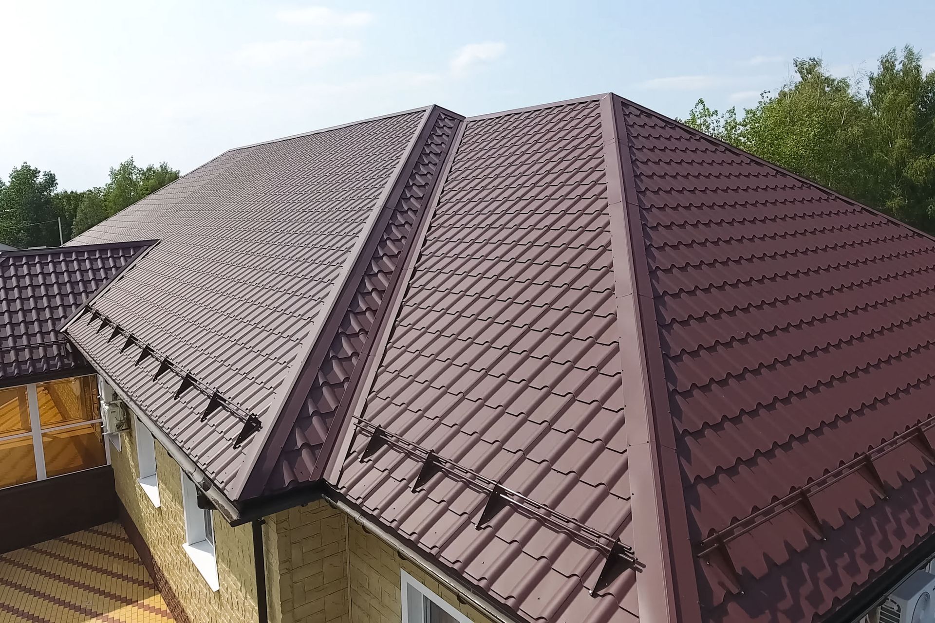 Aerial view of a brown metal roof with multiple gables and skylights surrounded by trees.