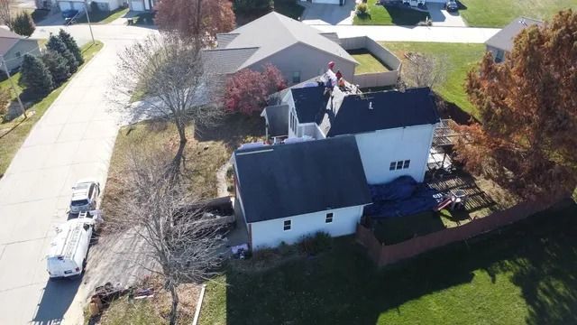 Aerial view of a white house with roof damage in a suburban neighborhood, with a truck parked nearby.