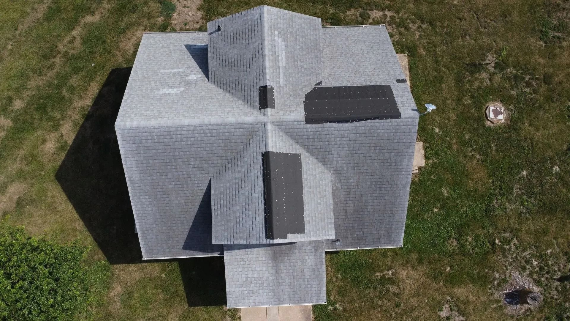 Aerial view of a gray house roof with several dormers, a small front porch, and grass yard surrounding it