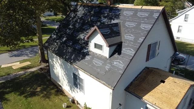 White house roof with gray shingles and a dormer, seen from above in a leafy residential area