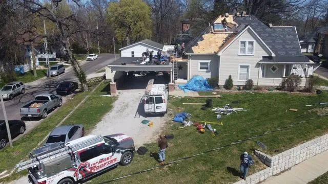 Residential house with open driveway, parked work vehicles, and scattered tools on the lawn