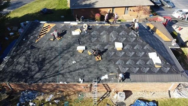 Roofers installing shingles on a large house roof with supplies and tools scattered across the surface.