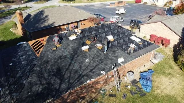 Roof under repair with workers, black underlayment, tools, and materials spread across the surface.