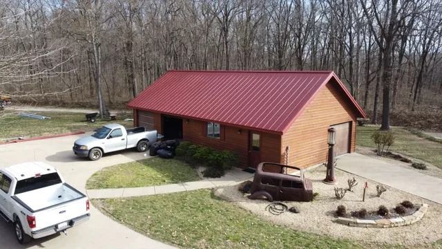 A red-roofed wooden building with parked trucks and a fire pit in a wooded yard.