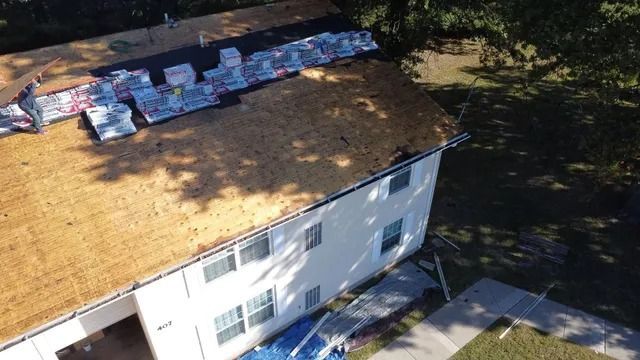 Aerial view of a house roof with scattered shingles and construction materials in sunlight