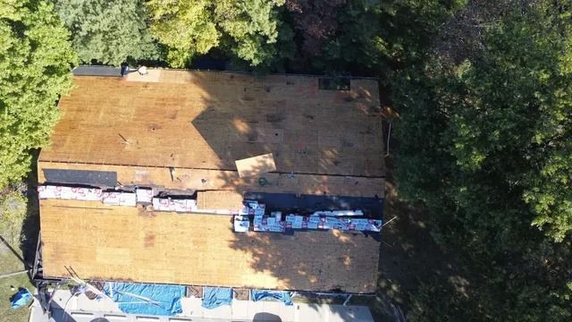 Aerial view of a tan-roofed building surrounded by dense green trees, with a vehicle parked beside it.
