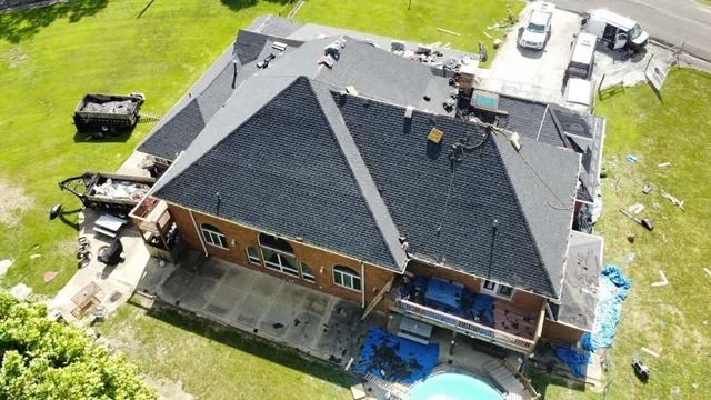 Aerial view of a house with a dark roof, backyard, and construction materials around it