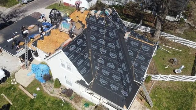 Aerial view of a house with a black roof under repair, surrounded by workers and construction materials.