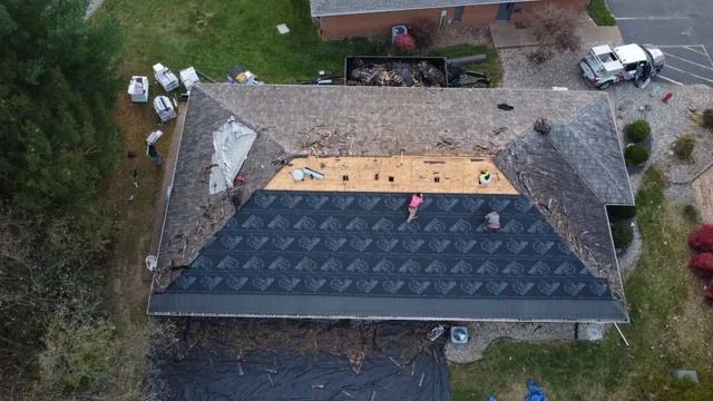 Aerial view of a house roof undergoing repair, with exposed plywood and shingles removed.
