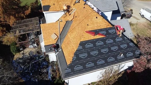 Aerial view of roofers installing black shingles on a house roof with orange underlayment.