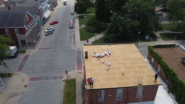 Aerial view of people on a tan rooftop beside a street and brick buildings.