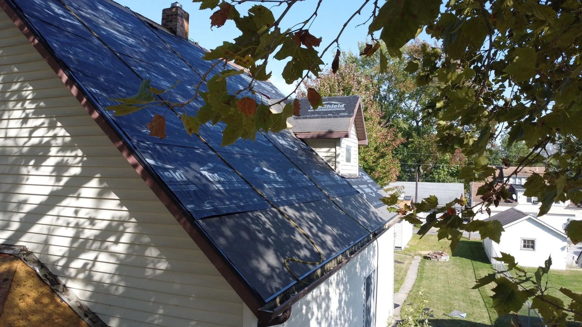 House with a blue roof beside trees and a grassy yard on a sunny day