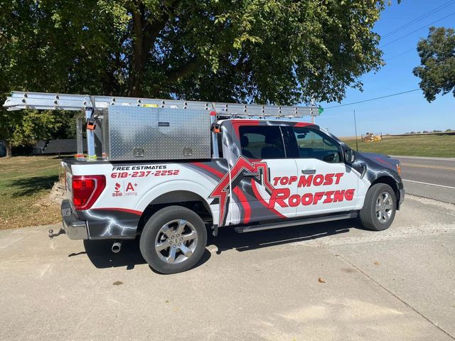 Red and white Top Notch Roofing pickup truck parked on a driveway beside a tree.