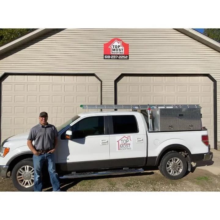 Worker standing beside a white pickup truck in front of a garage with a company sign