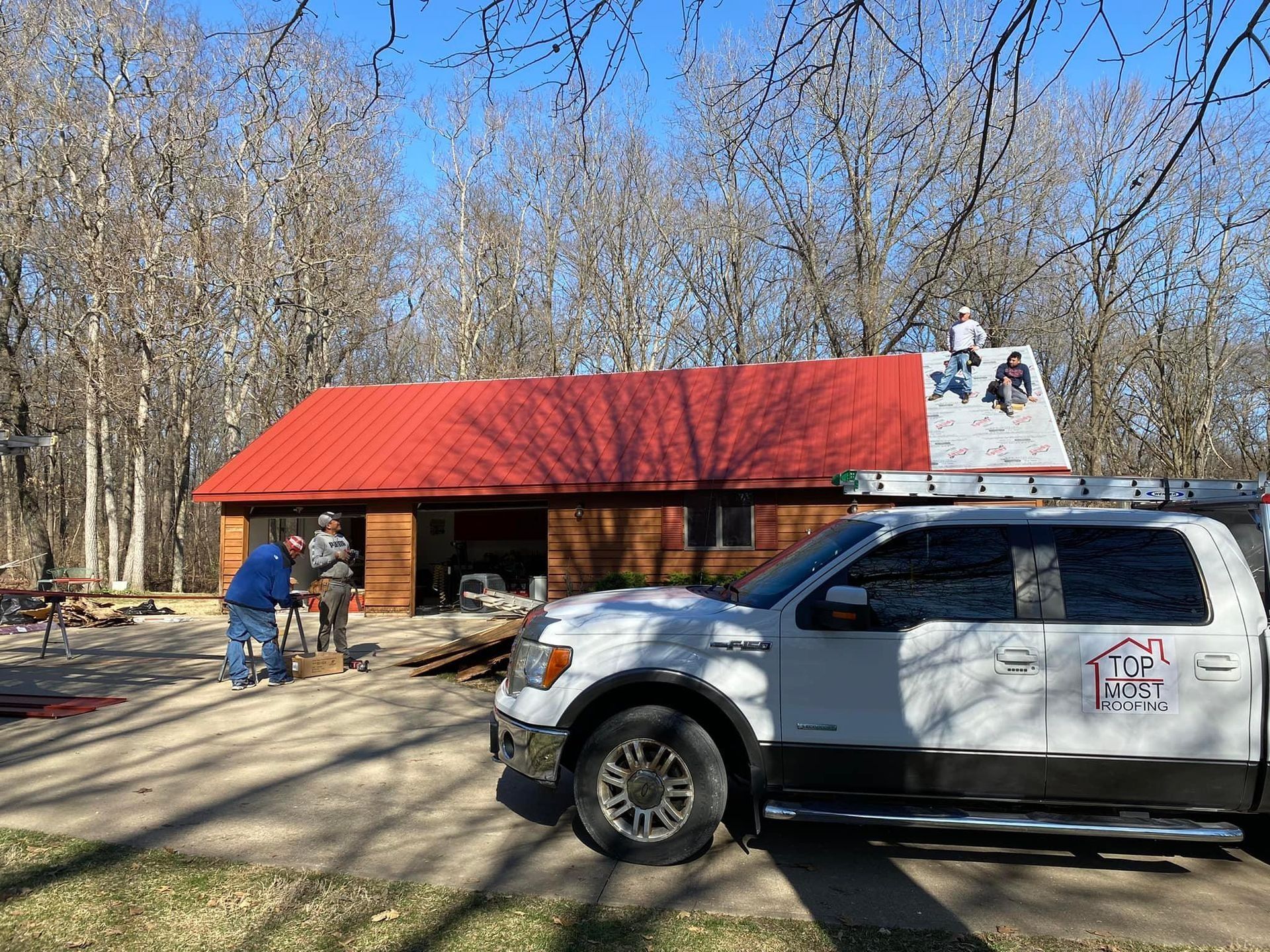 Red-roof pavilion in a wooded park with two people nearby and a white SUV in the foreground.