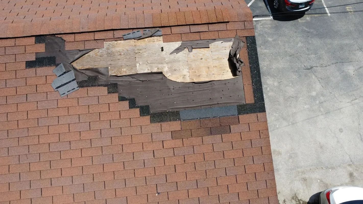 Damaged roof with missing shingles and exposed underlayment beside a paved driveway