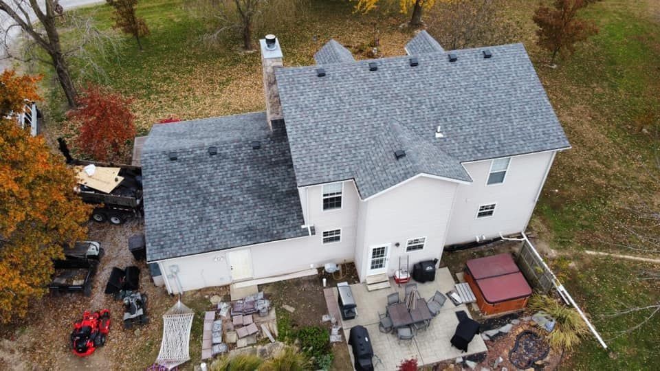 Aerial view of a white two-story house with a gray roof, patio furniture, and autumn trees around it