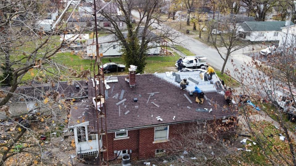 Aerial view of a damaged brick house with debris on the roof and emergency workers nearby