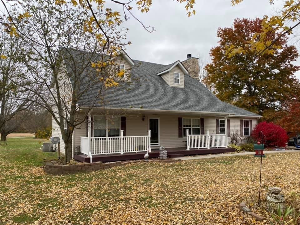 Single-story house with gray roof, white porch, and fallen autumn leaves in the yard