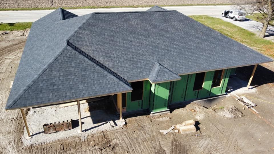 Aerial view of a house under construction with a dark gray roof and green exterior walls.