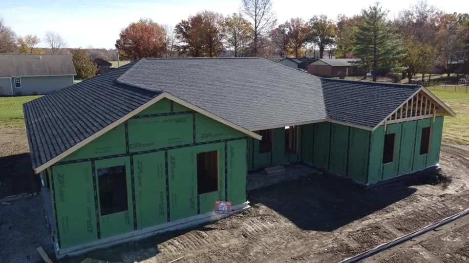 Green house exterior under construction with dark roof and unfinished siding on a dirt lot