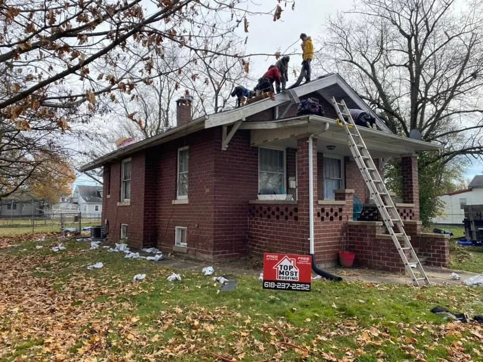 Workers repair a brick house roof with ladders and debris in the yard.