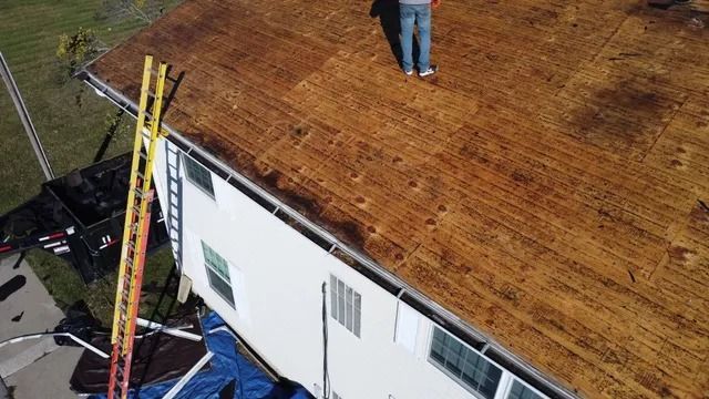 Roofing crew on a brown roof, with ladders and a worker standing near the ridge