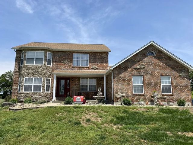 Two-story stone house with a gabled wing, front porch, and a red cooler on the lawn.