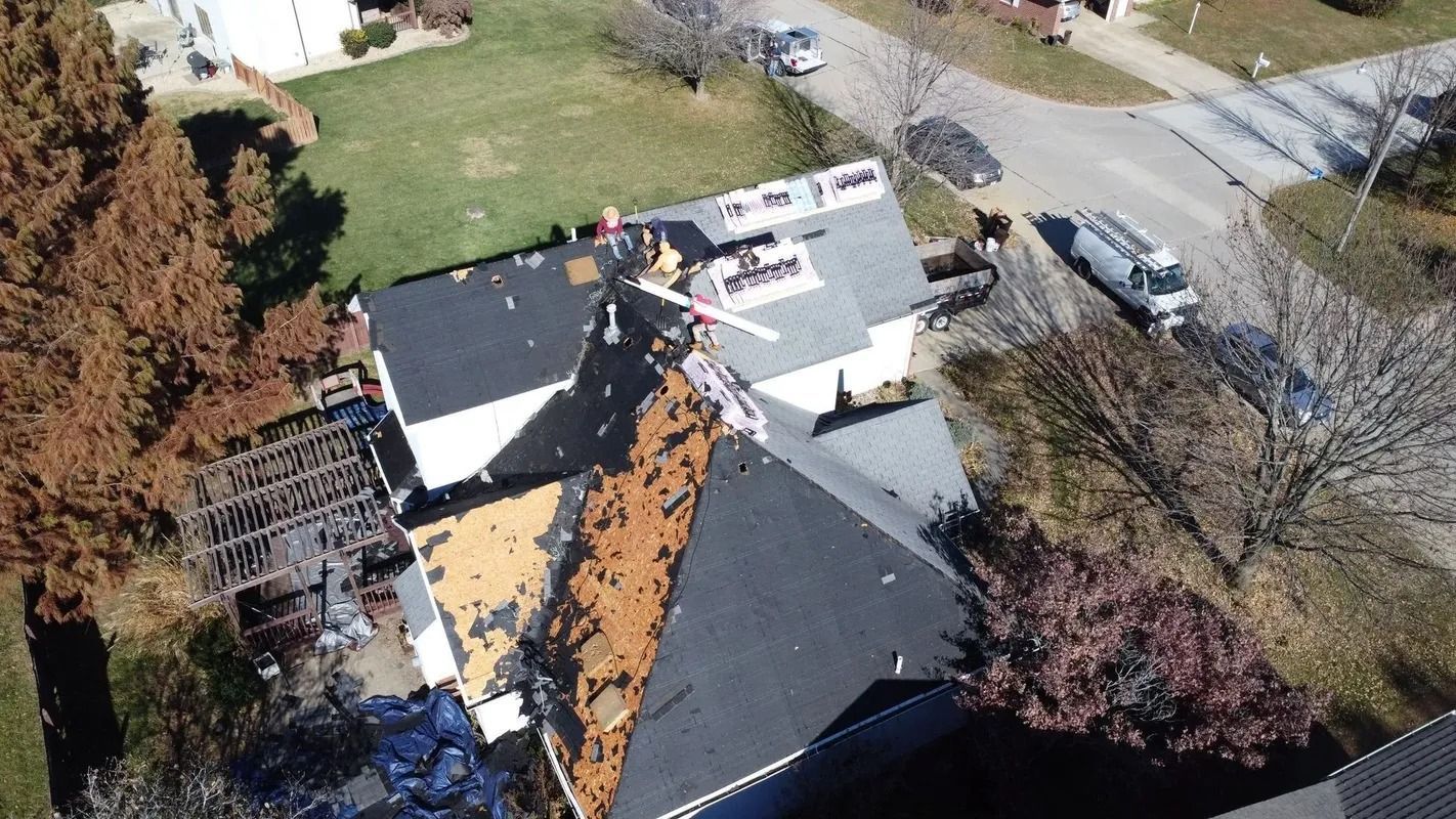 Aerial view of a house roof with workers doing repairs near a tree-lined street