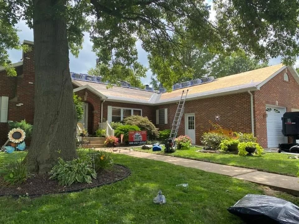 Brick house with a front porch, large tree, manicured lawn, and colorful garden beds