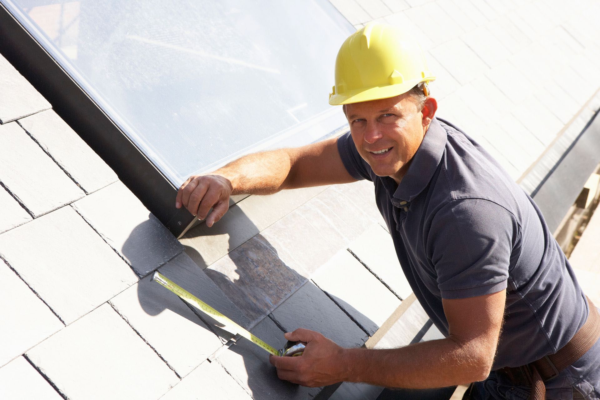 Worker in yellow hard hat measuring roof tiles with a tape measure