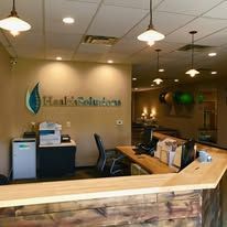 Reception desk in a well-lit office. Countertop is wood, with a health solutions logo on the wall.