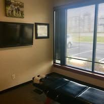 A chiropractor's office with a treatment table, TV, window, and a photo on the wall.