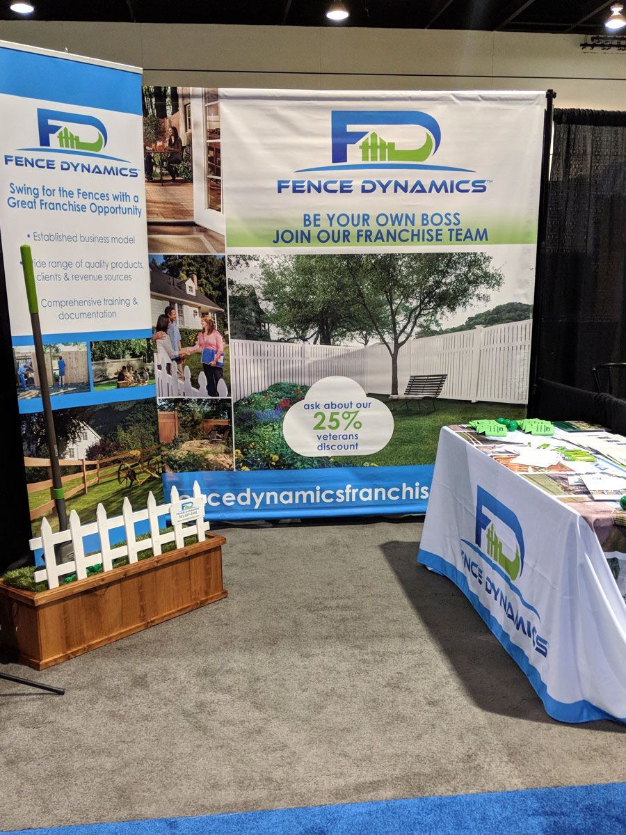 Trade show booth for Fence Dynamics with banners, brochures, and a small white picket fence display.