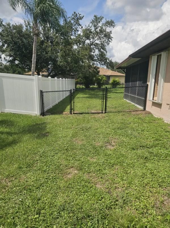 Backyard with green lawn, white fence, gate, and house exterior under a partly cloudy sky