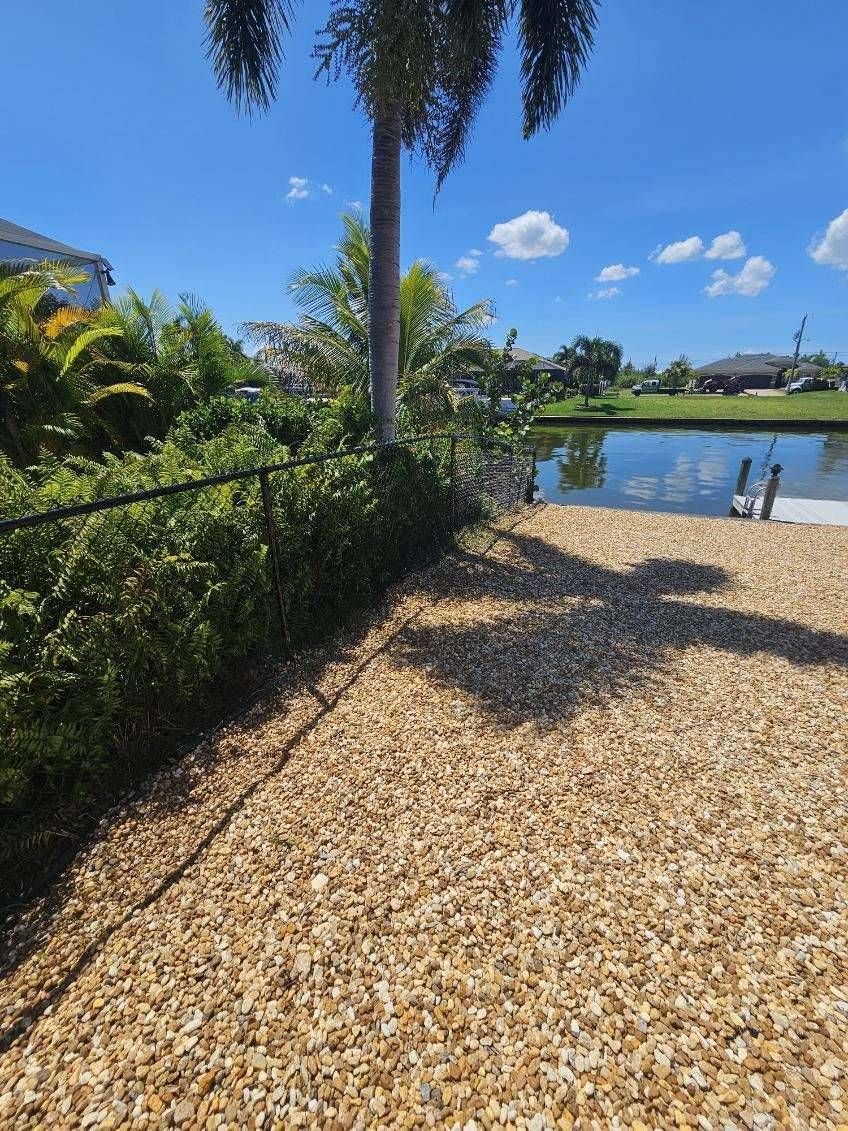 Backyard with chain link fence surrounded by trees and bushes with rock and a small white dock