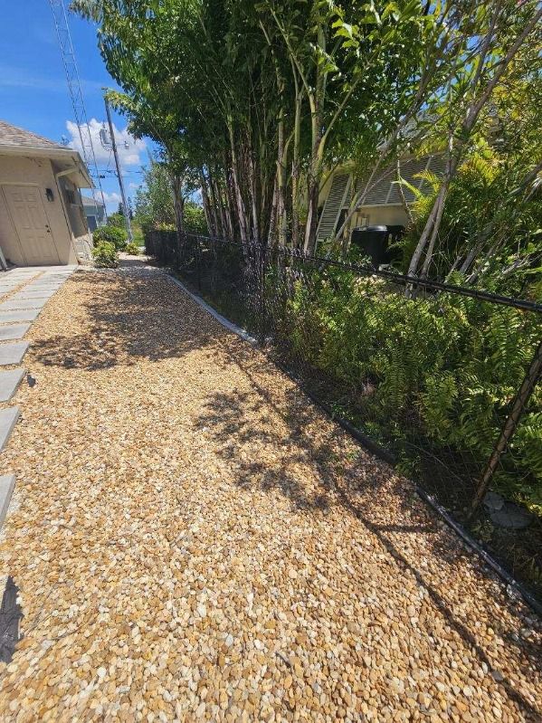Backyard with  tan house, cement stepping bricks, chain link fence surrounded by trees and bushes with rock 