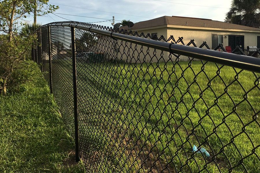 Chain-link fence beside a grassy yard with a building and people in the background