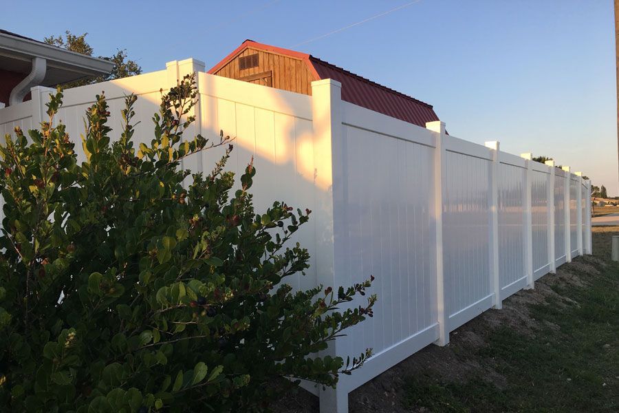 White vinyl fence along a grassy yard beside a house at sunset