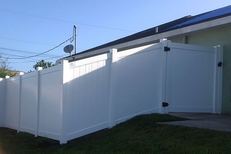 White vinyl fence and gate beside a house on a sunny day