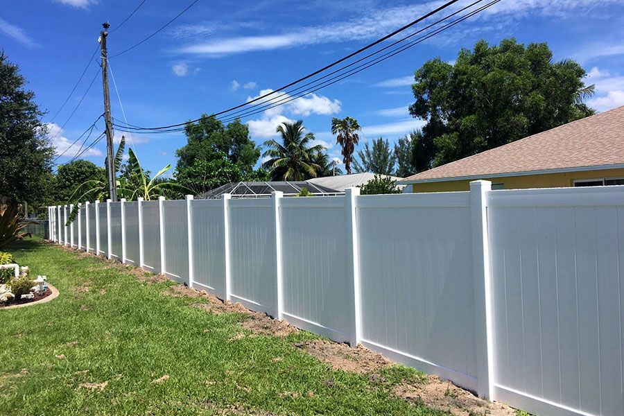 White vinyl privacy fence along a grassy yard under a blue sky with power lines and trees
