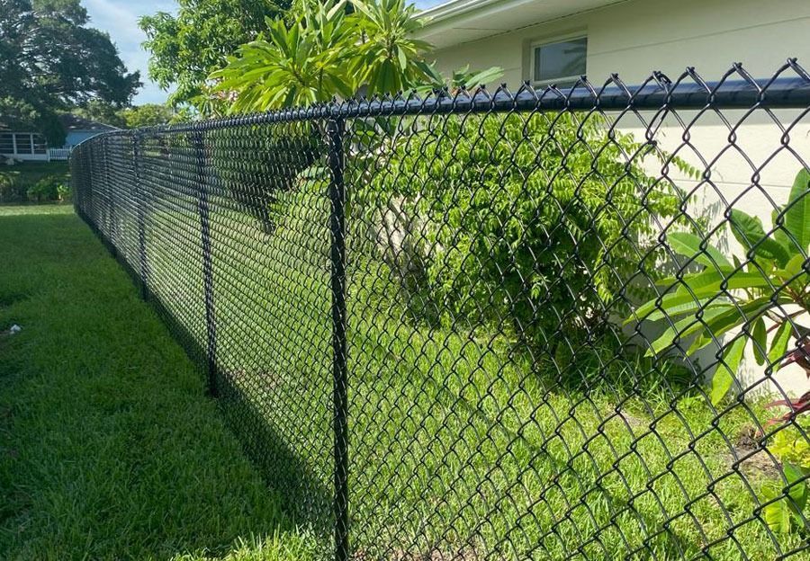 Black chain-link fence along a green lawn beside a house and shrubs