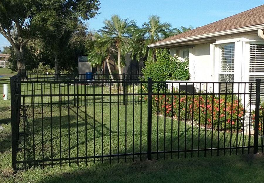Black metal fence in front of a white house with palm trees and a green lawn