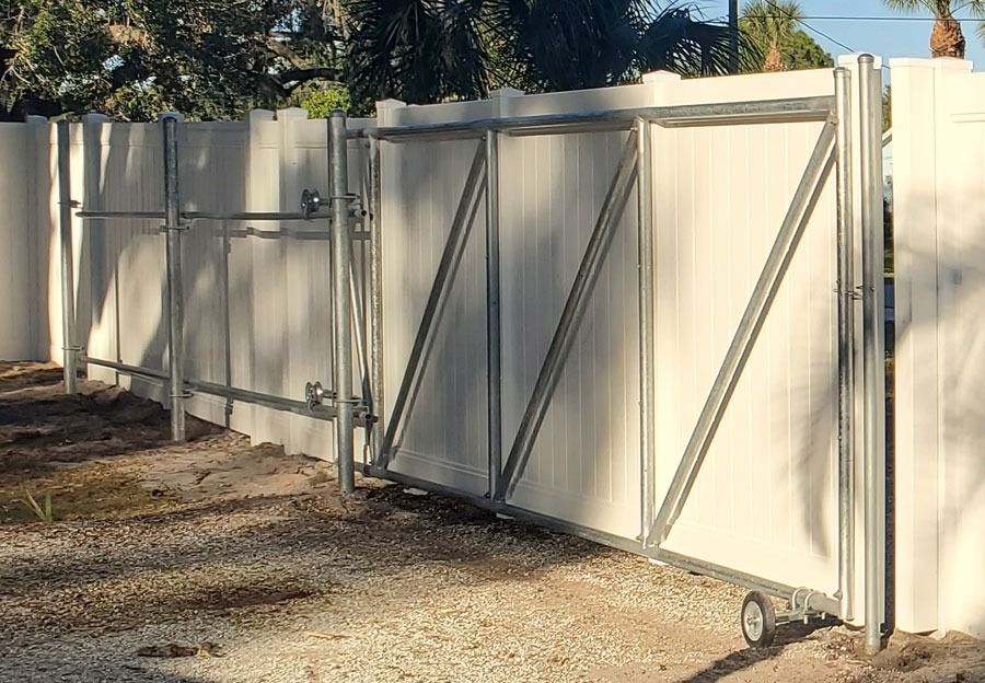White metal privacy fence with a double gate along a dirt driveway outdoors
