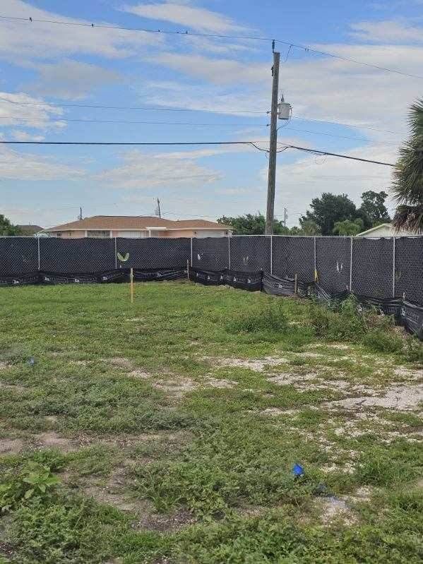 Empty grassy backyard with chain-link fence, utility pole, and blue sky with scattered clouds.
